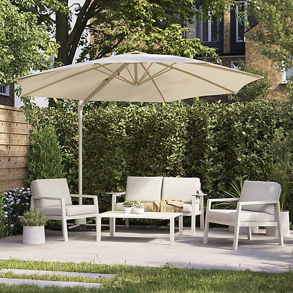 Outdoor patio set with cream umbrella, chairs, and table in a garden setting.